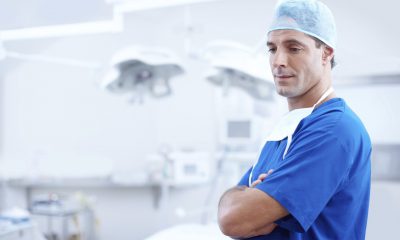 doktor stojący w gabinecie; ubrany w niebieski kitel i czepek lekarski