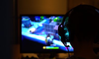 mężczyzna grający na komputerze w grę komputerową; ma na sobie słuchawki, na ekranie widać rozgrywkę