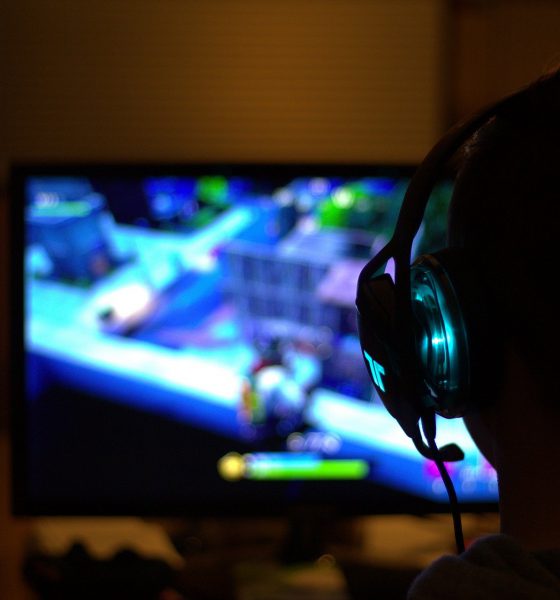 mężczyzna grający na komputerze w grę komputerową; ma na sobie słuchawki, na ekranie widać rozgrywkę